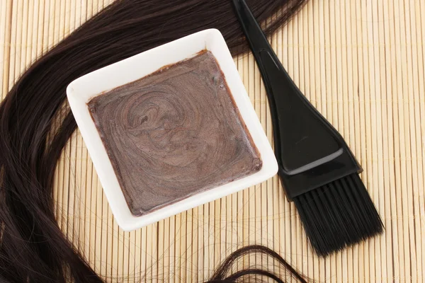 Tintura de cabelo na tigela e escova para coloração de cabelo no tapete de bambu bege, close-up — Fotografia de Stock