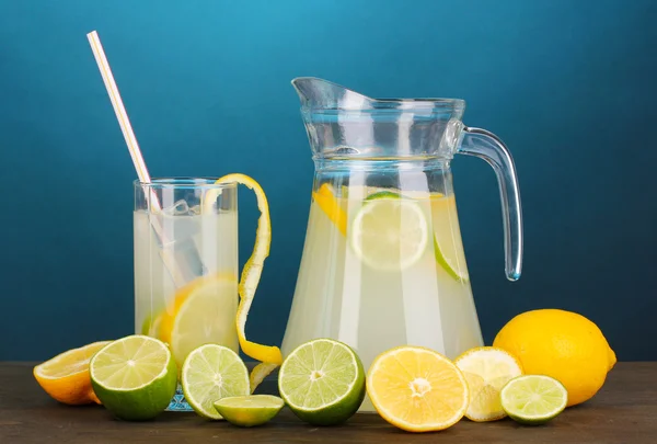 Citrus limonade in werper en glas van citrus rond op houten tafel op blauwe achtergrond — Stockfoto