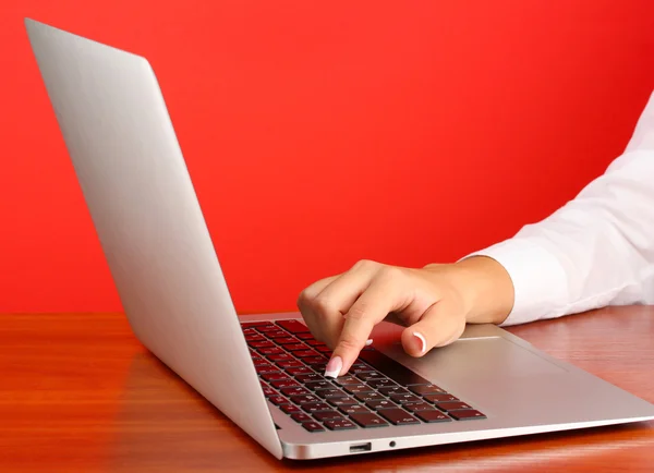 Las manos de la mujer de negocios escribiendo en el ordenador portátil, sobre fondo rojo primer plano —  Fotos de Stock