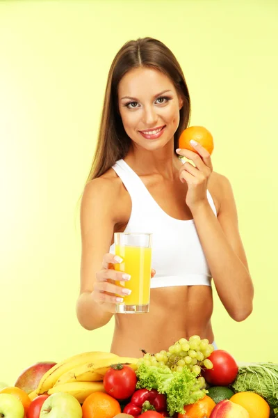 Bella giovane donna con frutta e verdura e bicchiere di succo, su sfondo verde — Foto Stock