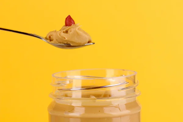 Delicious peanut butter in jar and spoon on yellow background — Stock Photo, Image