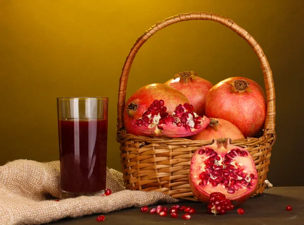 Zralé granátová jablka na koši se sklenicí jablečného džusu na dřevěném stole na žlutém pozadí — Stock fotografie