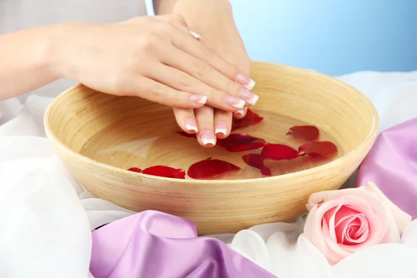 Manos de mujer con cuenco de madera de agua con pétalos, sobre fondo azul — Foto de Stock