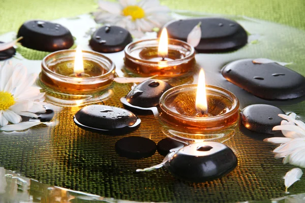 Курортные камни с цветами и свечами в воде на тарелке — стоковое фото