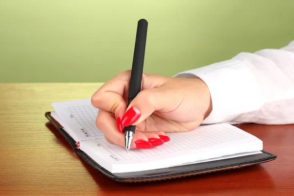 Hand signing in notebook on wooden table on color background — Stock Photo, Image