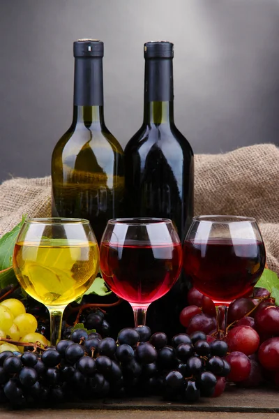 Μπουκάλια και ποτήρια κρασί και σταφύλια σε γκρι φόντο — Φωτογραφία Αρχείου