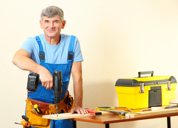 Builder drills board on table on wall background
