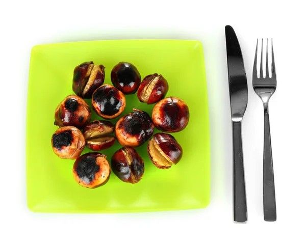 Roasted chestnuts in the green plate with fork and knife isolated on white Stock Photo