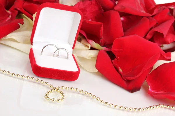 Belle boîte avec anneaux de mariage sur fond de pétales de rose rouge, blanc et rose isolé sur fond blanc Image En Vente