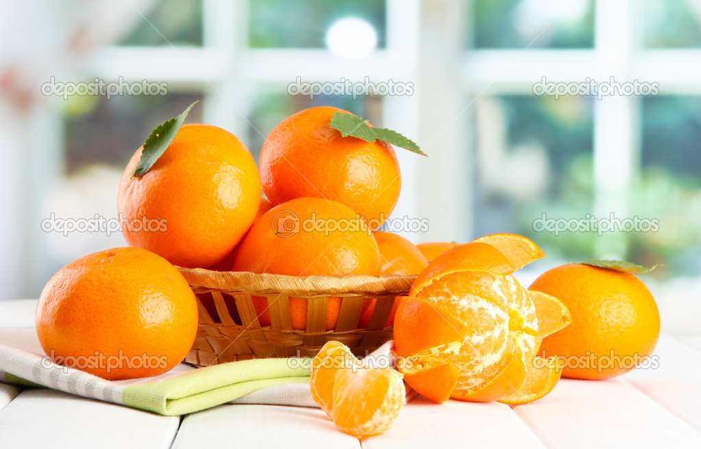tangerines with leaves in a beautiful basket, on wooden table on window background