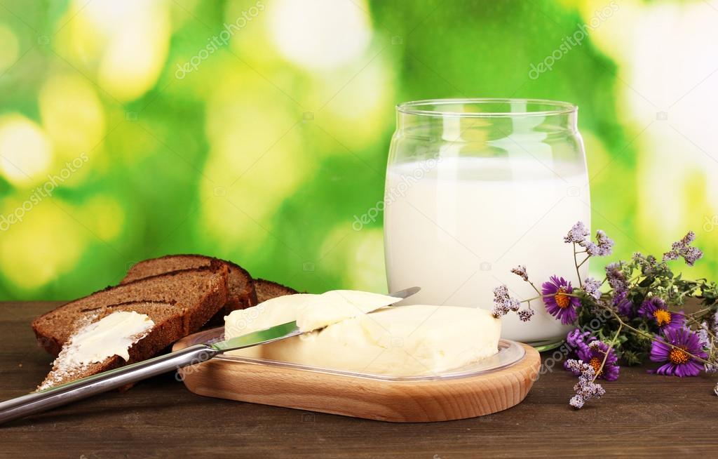 Butter on wooden holder surrounded by bread and milk on wooden table on natural background close-up