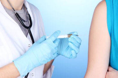 Doktor holding şırınga ile mavi arka plan üzerinde hastanın omuz içine aşı