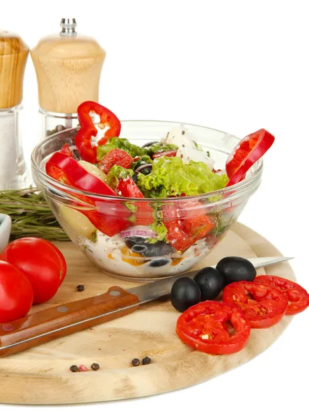 Fresh greek salad in glass bowl surrounded by ingredients for cooking isolated on white — Stock Photo, Image