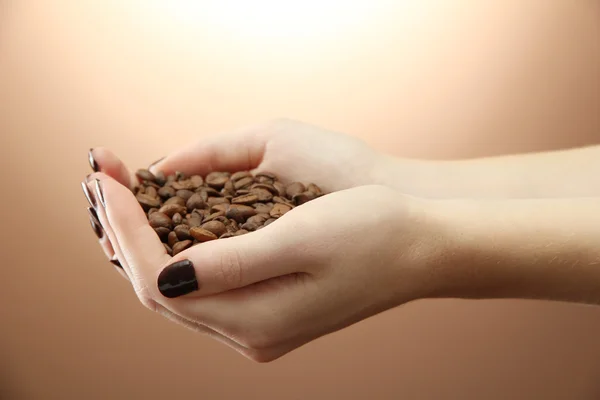 Kvinnliga händer med kaffebönor, på brun bakgrund — Stockfoto