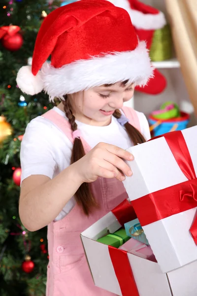 Una niña abre un regalo en una habitación festivamente decorada —  Fotos de Stock