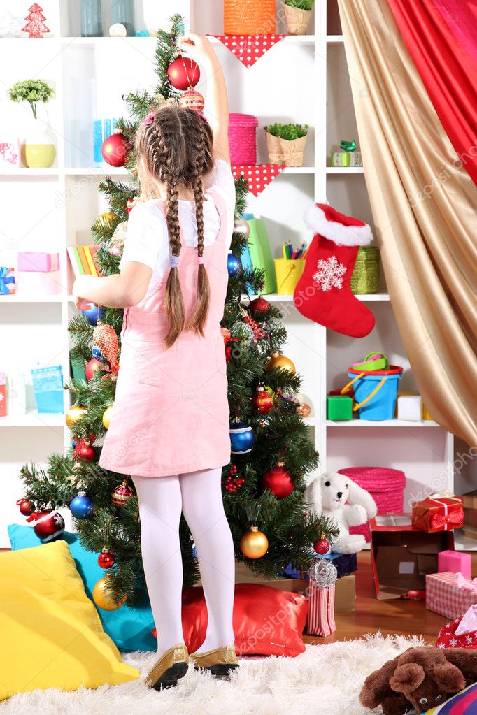 Little girl decorates Christmas tree in festively decorated room