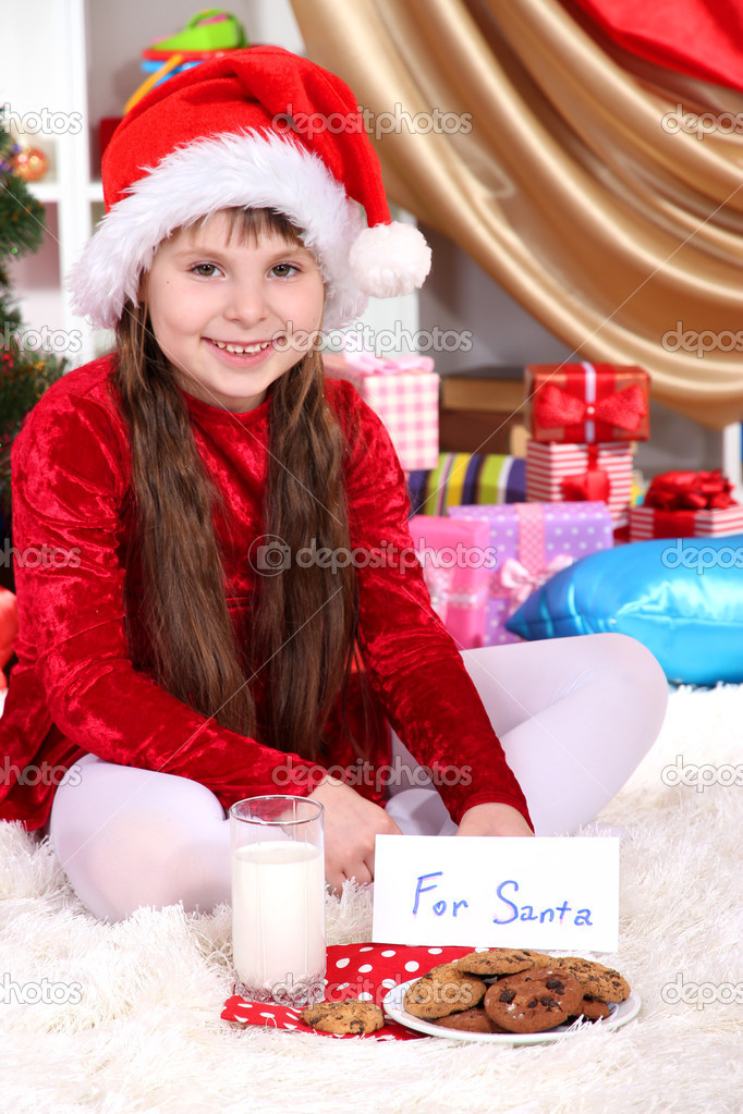 Beautiful little girl with milk and cookies for Santa Claus in festively decorated room