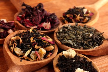 assortment of dry tea in spoons, on wooden background clipart