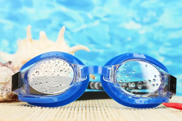 Blue swim goggles with drops on a bamboo pad, on blue sea background — Stock Photo, Image