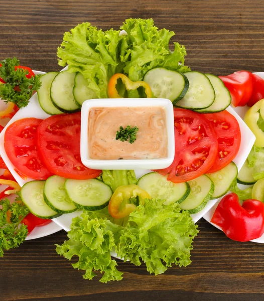 Gehacktes Gemüse und Soße auf Teller auf Holztisch — Stockfoto