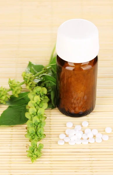 Flacone di medicinale con compresse e fiori su tappetino di bambù — Foto Stock