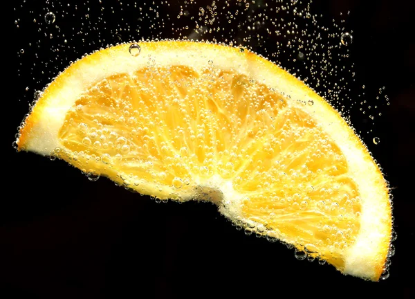 Fatia de laranja na água com bolhas, no fundo preto — Fotografia de Stock