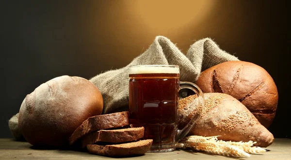 Tankard de pães de kvass e centeio com orelhas, na mesa de madeira no fundo marrom — Fotografia de Stock