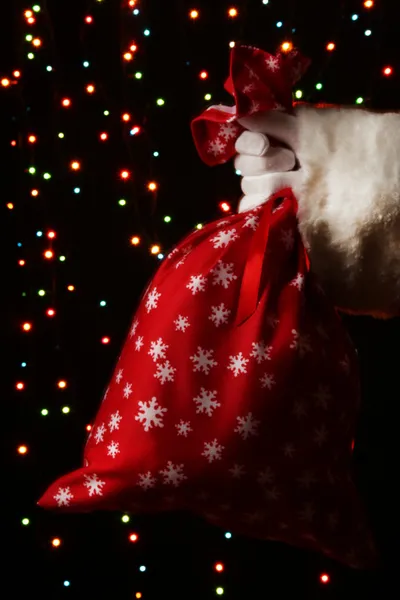 Santa Claus hand holding bag of gifts on bright background — Stock Photo, Image