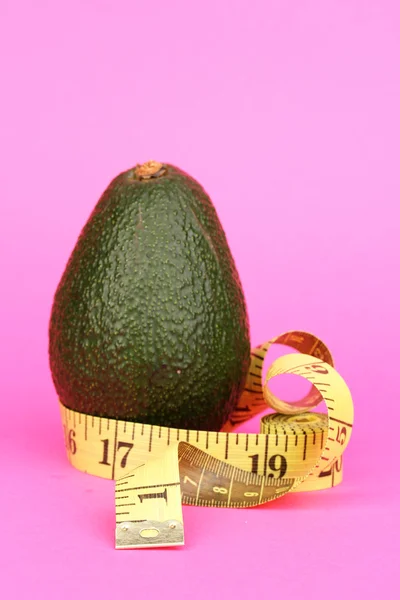 Aguacate con cinta métrica sobre fondo rosa — Foto de Stock