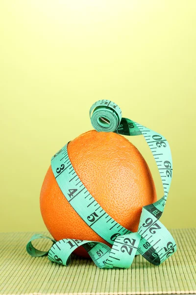 Orange with measuring tape on green background — Stock Photo, Image