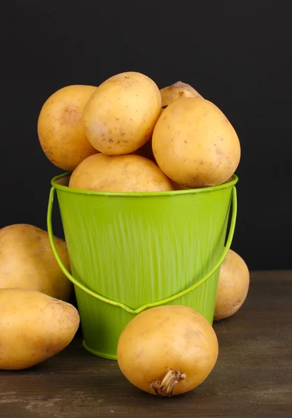 Ripe potatoes in pail on wooden table on black background — Stock Photo, Image