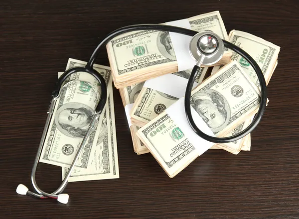 Concetto di costo sanitario: stetoscopio e dollari su fondo di legno — Foto Stock