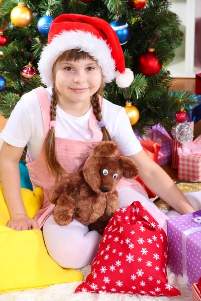 Κοριτσάκι με το καπέλο santa κοντά το χριστουγεννιάτικο δέντρο σε γιορτινή διακόσμηση δωμάτιο — Φωτογραφία Αρχείου