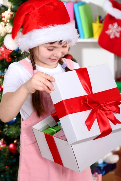 Egy kislány megnyílik egy ajándék ünnepélyesen feldíszített teremben — Stock Fotó