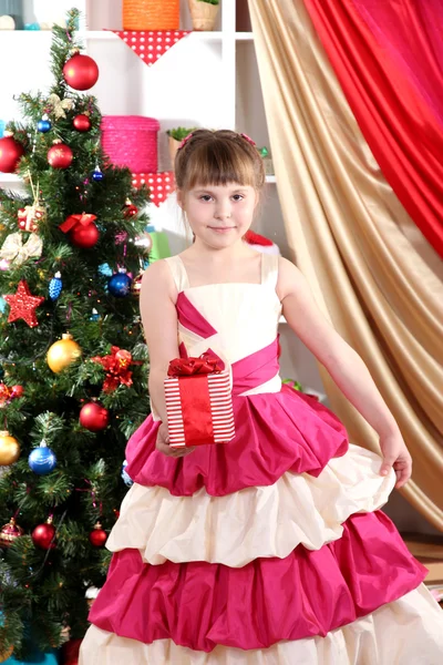 Menina bonita em vestido de férias com presente em suas mãos no quarto festivamente decorado — Fotografia de Stock