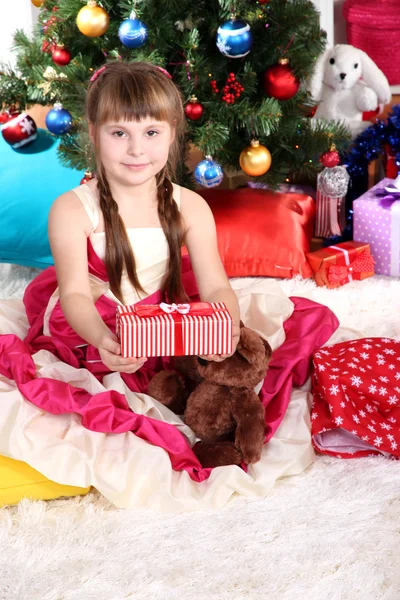 Vacker liten flicka i holiday klänning med gift i händerna i festligt dekorerade rum — Stockfoto