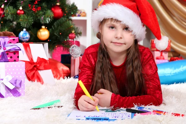 Menina bonita escreve carta ao Papai Noel em quarto festivamente decorado — Fotografia de Stock