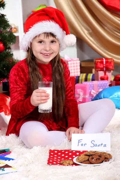 Belle petite fille avec du lait et des biscuits pour le Père Noël dans une chambre décorée de façon festive — Photo