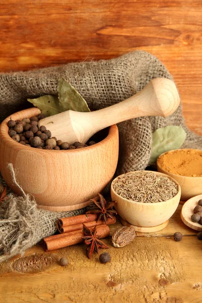 Mortar, bowls and spoons with spices, on wooden background — Stock Photo, Image