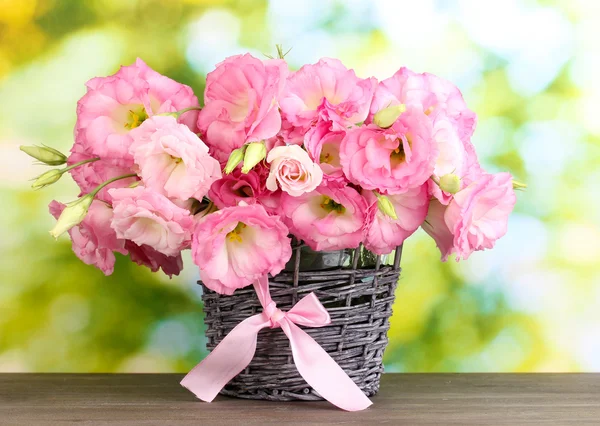 Bouquet of eustoma flowers in wicker vase, on wooden table, on green background — Stock Photo, Image