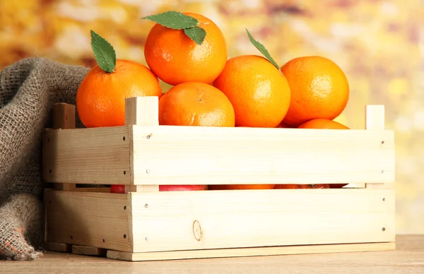 Ripe tasty tangerines with leaves in wooden box on table on orange background — Stock Photo, Image
