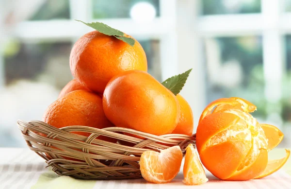 Tangerines with leaves in a beautiful basket, on table on window background — Stock Photo, Image