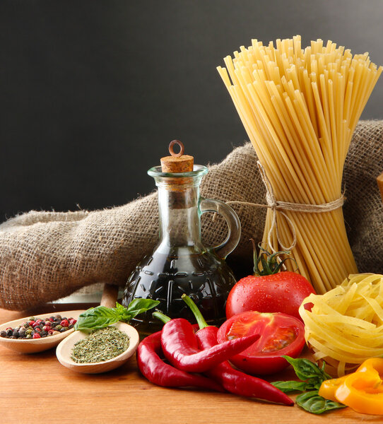 Pasta spaghetti, vegetables and spices, on wooden table, on grey background