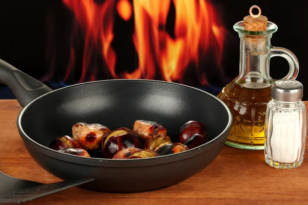 Pečené kaštany v pánvi a karafy s olejem, solí a pepřem na dřevěný stůl detail — Stock fotografie