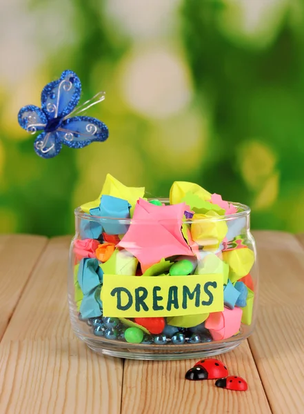 Glass vase with paper stars with dreams on wooden table on natural background — Stock Photo, Image
