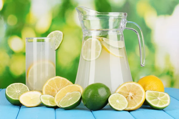 Цитрусовый лимонад в кувшине и стакан цитрусовых вокруг на естественном деревянном столе на голубом фоне — стоковое фото
