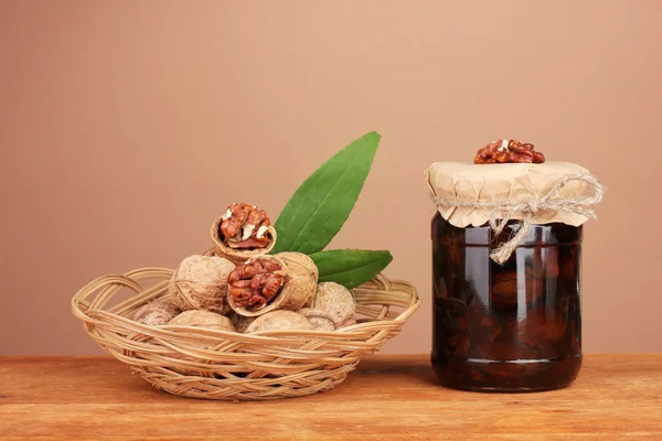 Marmellata-vaso di noci su tavolo di legno e un cesto con noci su sfondo marrone — Foto Stock