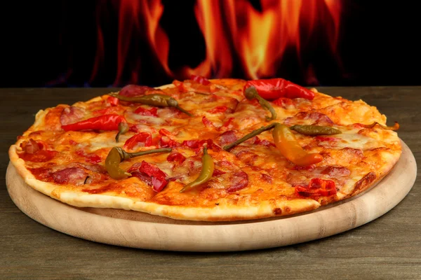 Tasty pepperoni pizza on wooden board on flame background — Stock Photo, Image