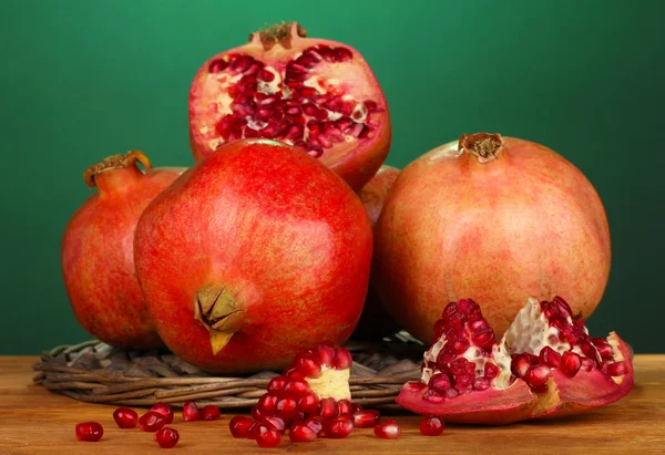 Ripe pomegranates on wicker cradle on green background — Stock Photo, Image