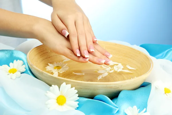 Manos de mujer con cuenco de madera de agua con flores, sobre fondo azul — Foto de Stock